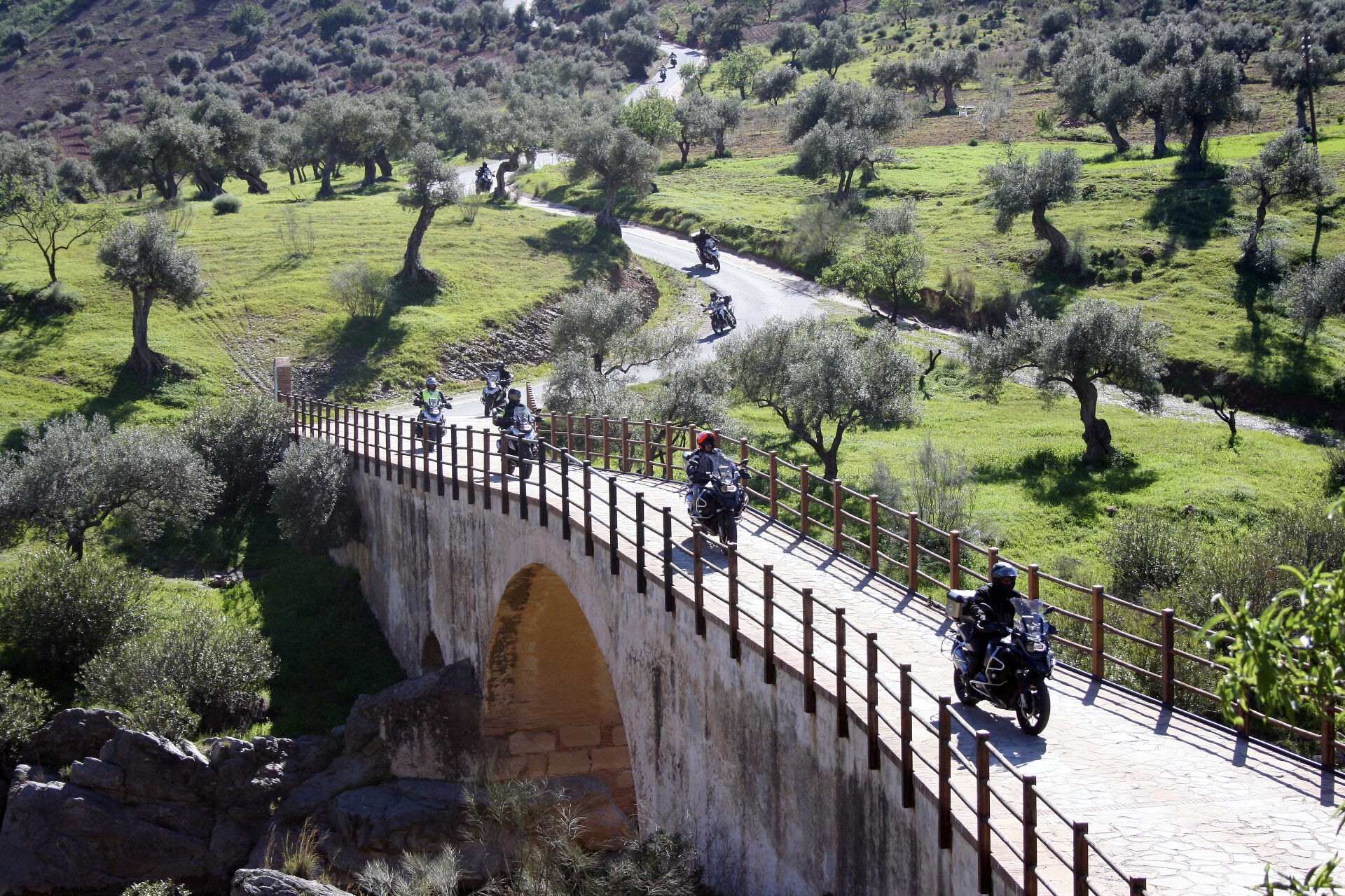 MC-förare korsar stenbro bland olivlundar i Andalusien
